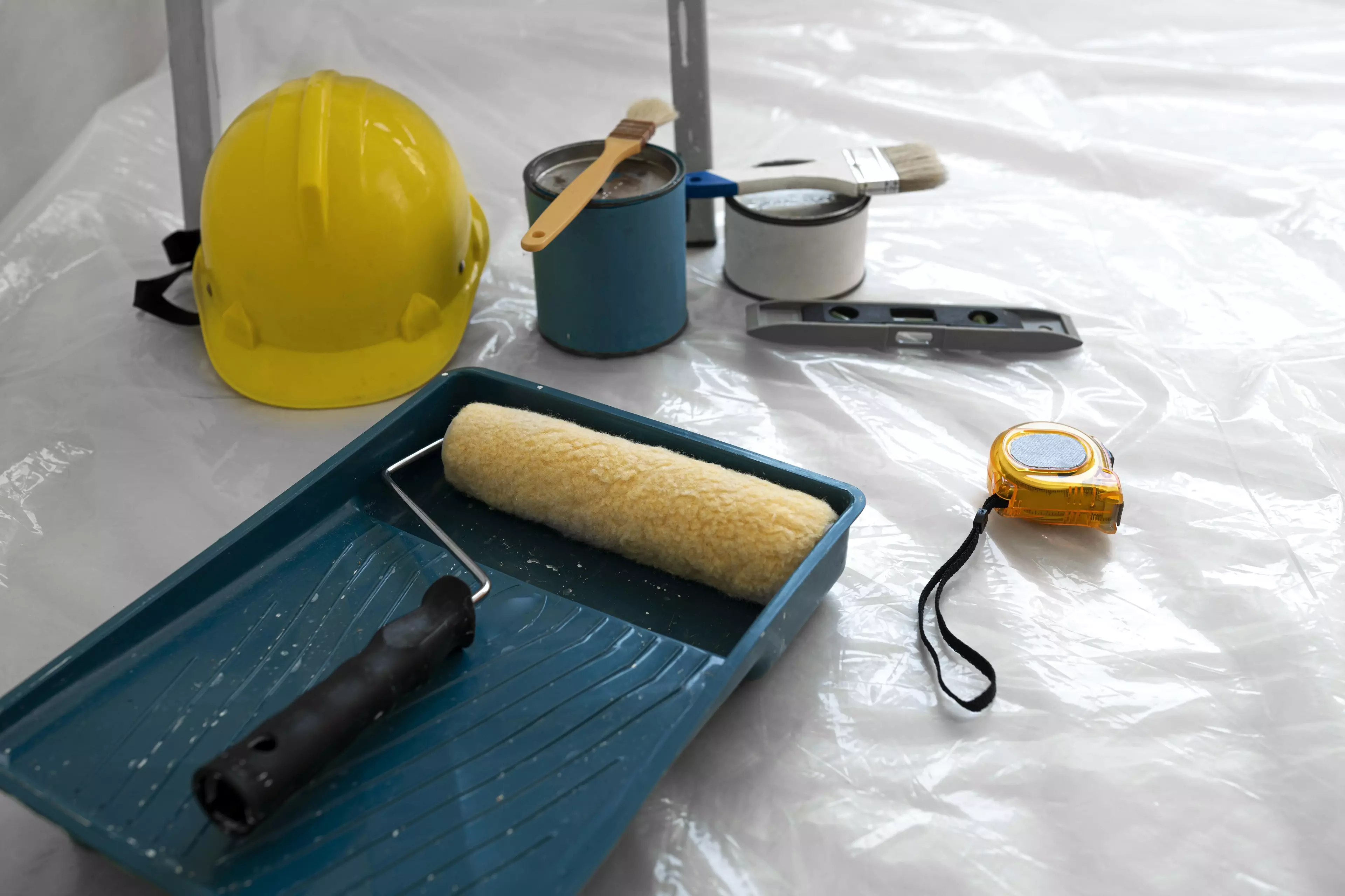 Painting materials on the floor with a yellow hardhat next to them.